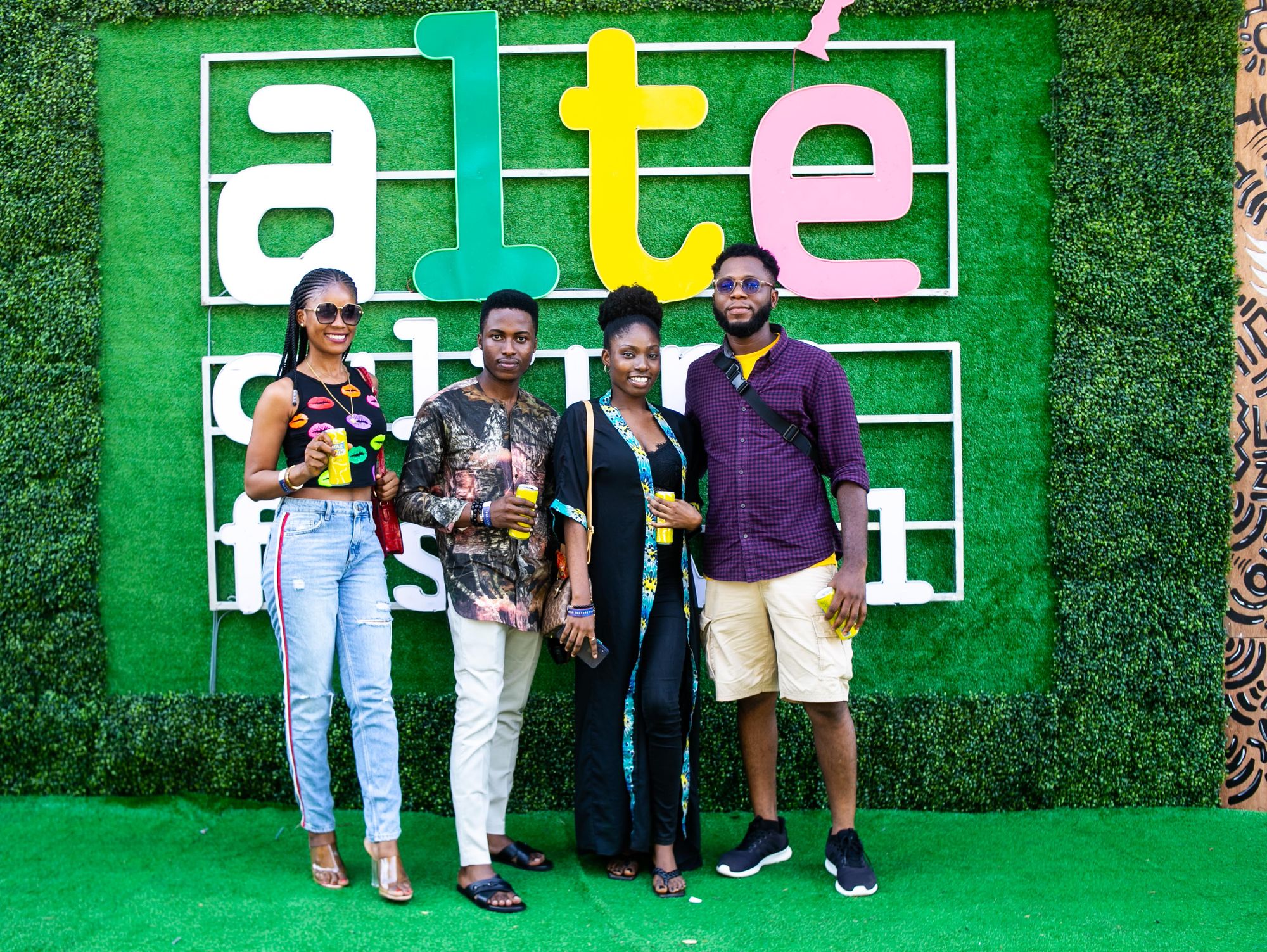 Two women and two men posing for pictures behind the Alté Culture Festival logo