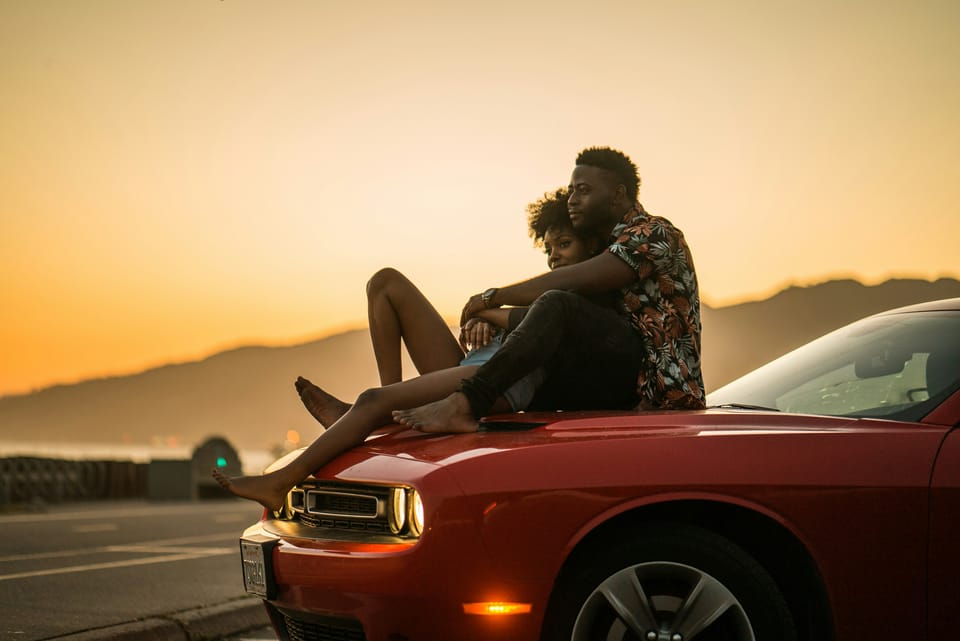 A black couple sitting on a red car